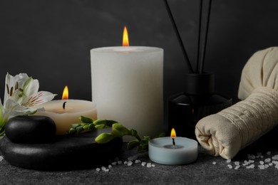 Photo of Beautiful spa composition with different care products and burning candles on dark grey table against black background