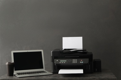 Modern printer with paper and laptop on grey table