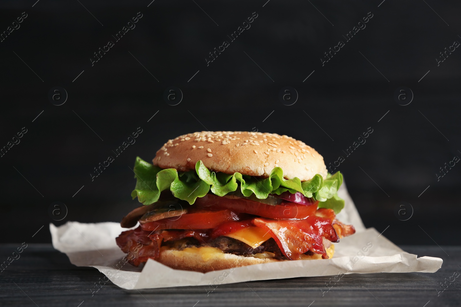 Photo of Tasty burger with bacon on wooden table