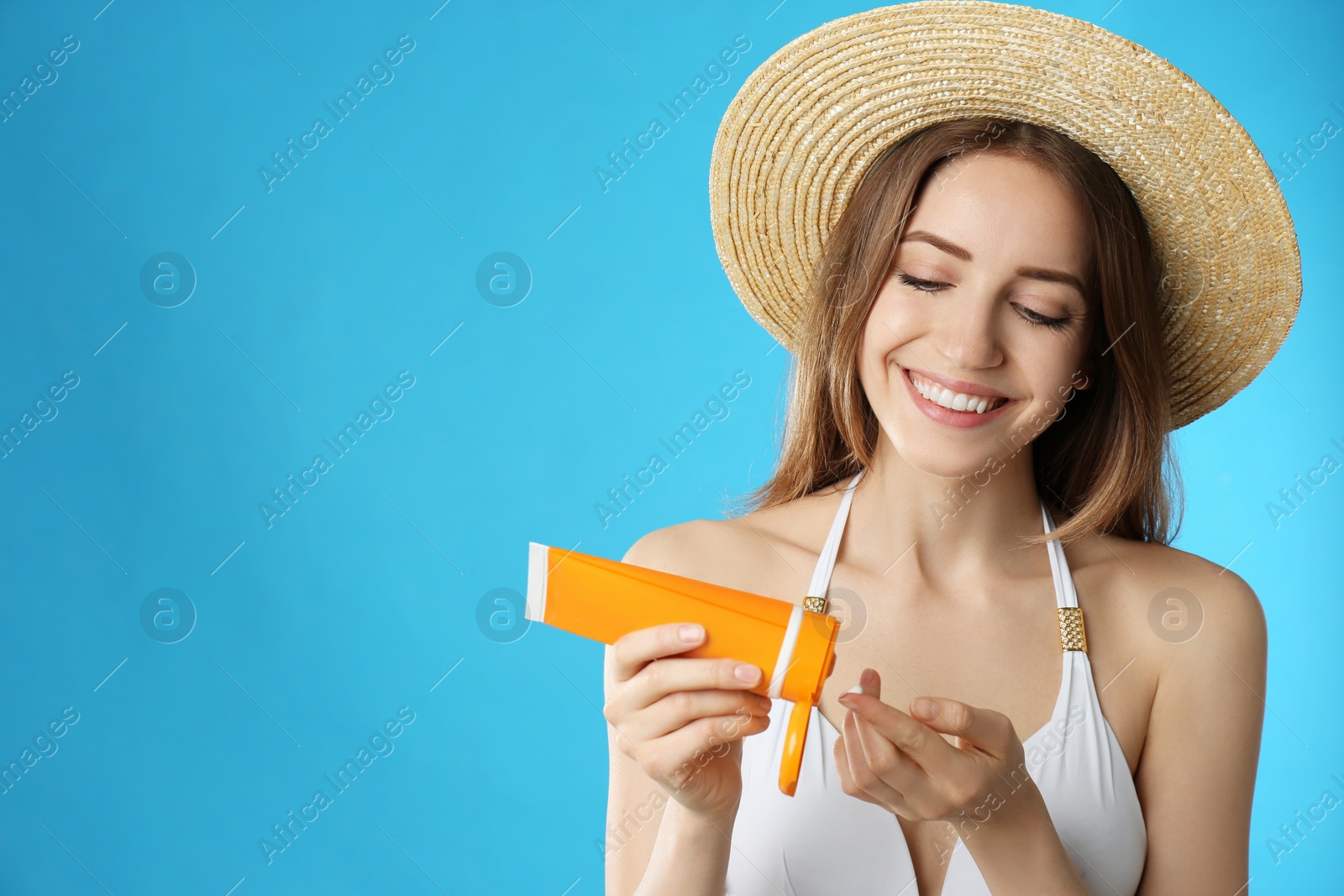 Photo of Young woman applying sun protection cream on light blue background. Space for text