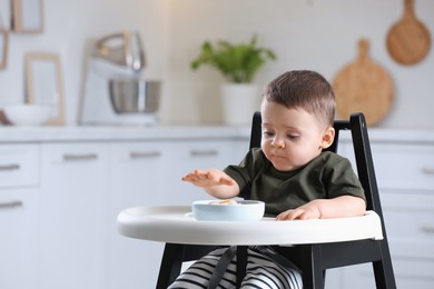 Cute little baby eating healthy food in high chair at home. Space for text