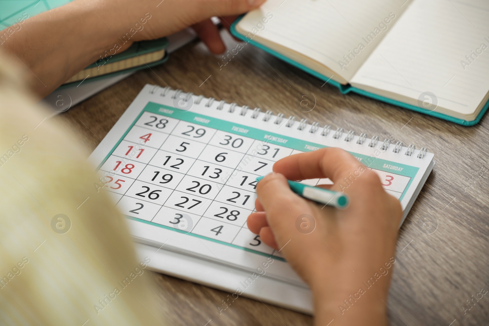 Photo of Woman marking date in calendar at wooden table, closeup