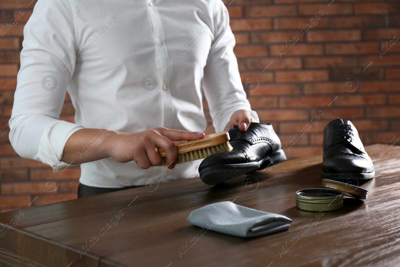 Photo of Man cleaning leather shoe at wooden table indoors, closeup