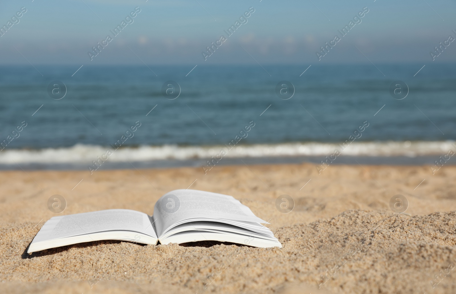 Photo of Open book on sandy beach near sea. Space for text