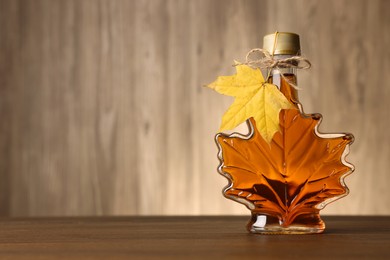 Photo of Leaf shaped bottle of tasty maple syrup on wooden table. Space for text