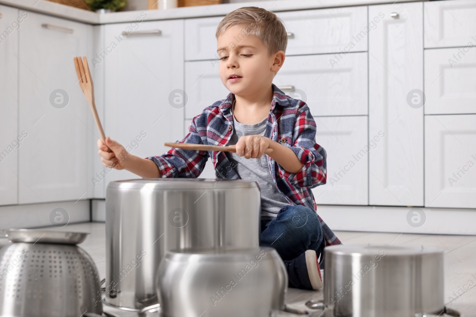 Photo of Little boy pretending to play drums on pots in kitchen