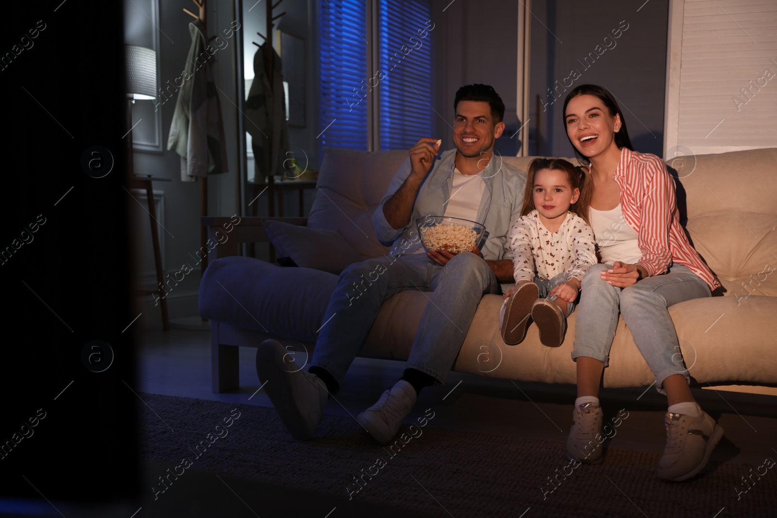 Photo of Family watching movie with popcorn on sofa at night, space for text