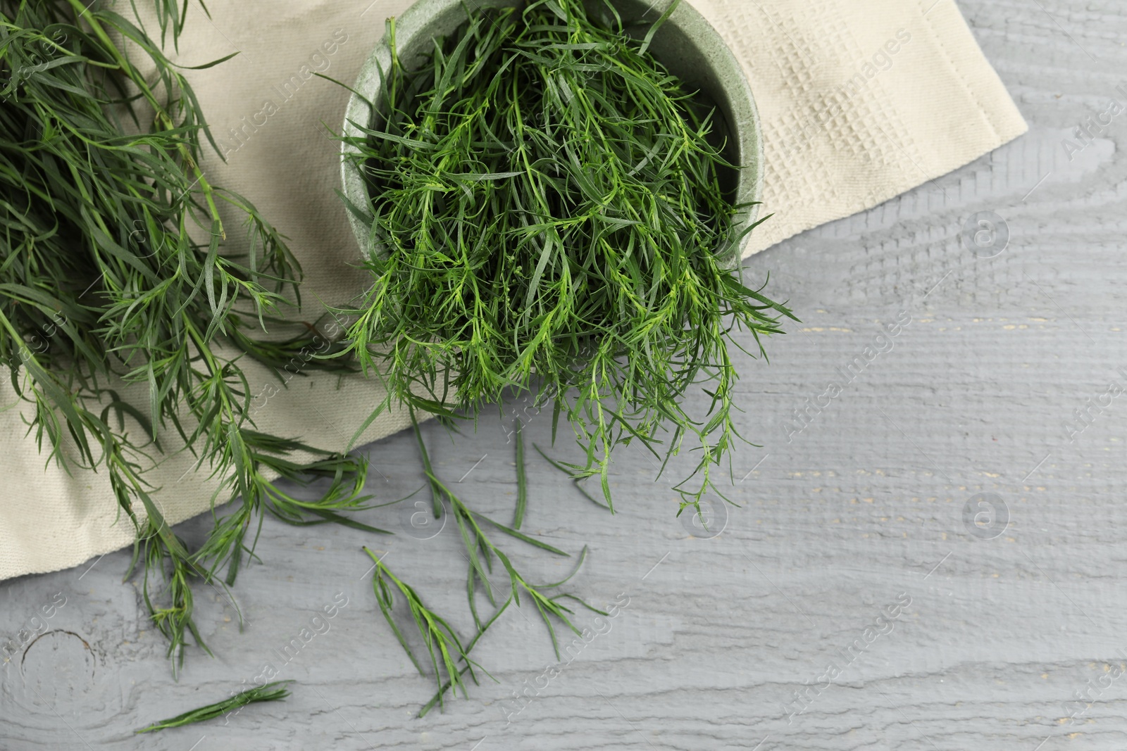 Photo of Fresh tarragon leaves on grey wooden table, flat lay. Space for text