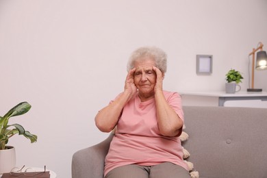 Senior woman with headache sitting on sofa at home