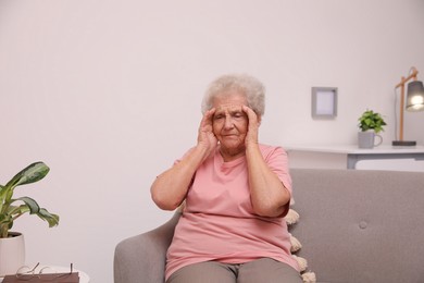 Photo of Senior woman with headache sitting on sofa at home