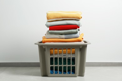 Photo of Plastic laundry basket with clean clothes on floor indoors