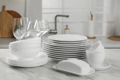 Photo of Clean plates, bowls, cups and glasses on white marble table in kitchen