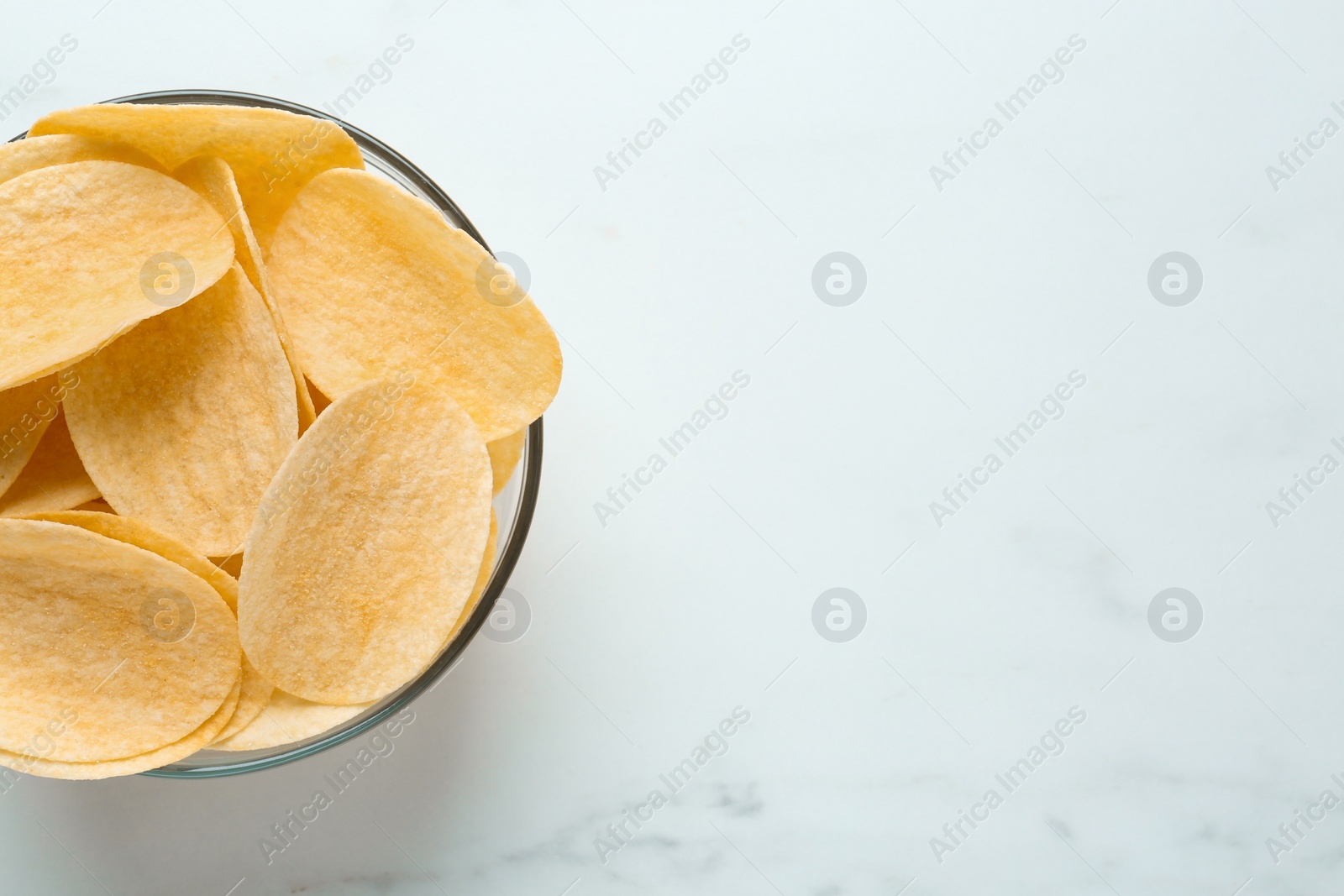 Photo of Bowl with delicious potato chips on white marble table, top view. Space for text