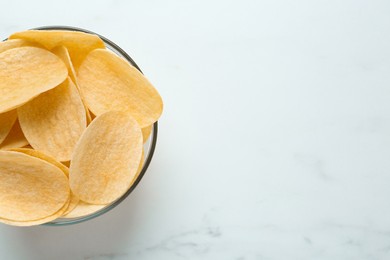 Photo of Bowl with delicious potato chips on white marble table, top view. Space for text