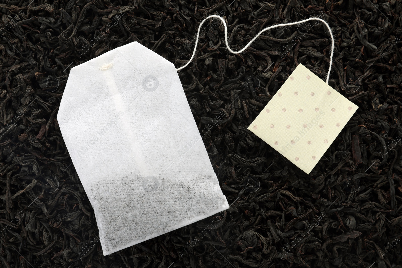 Photo of Unused tea bag with tag on dry leaves, top view. Space for text