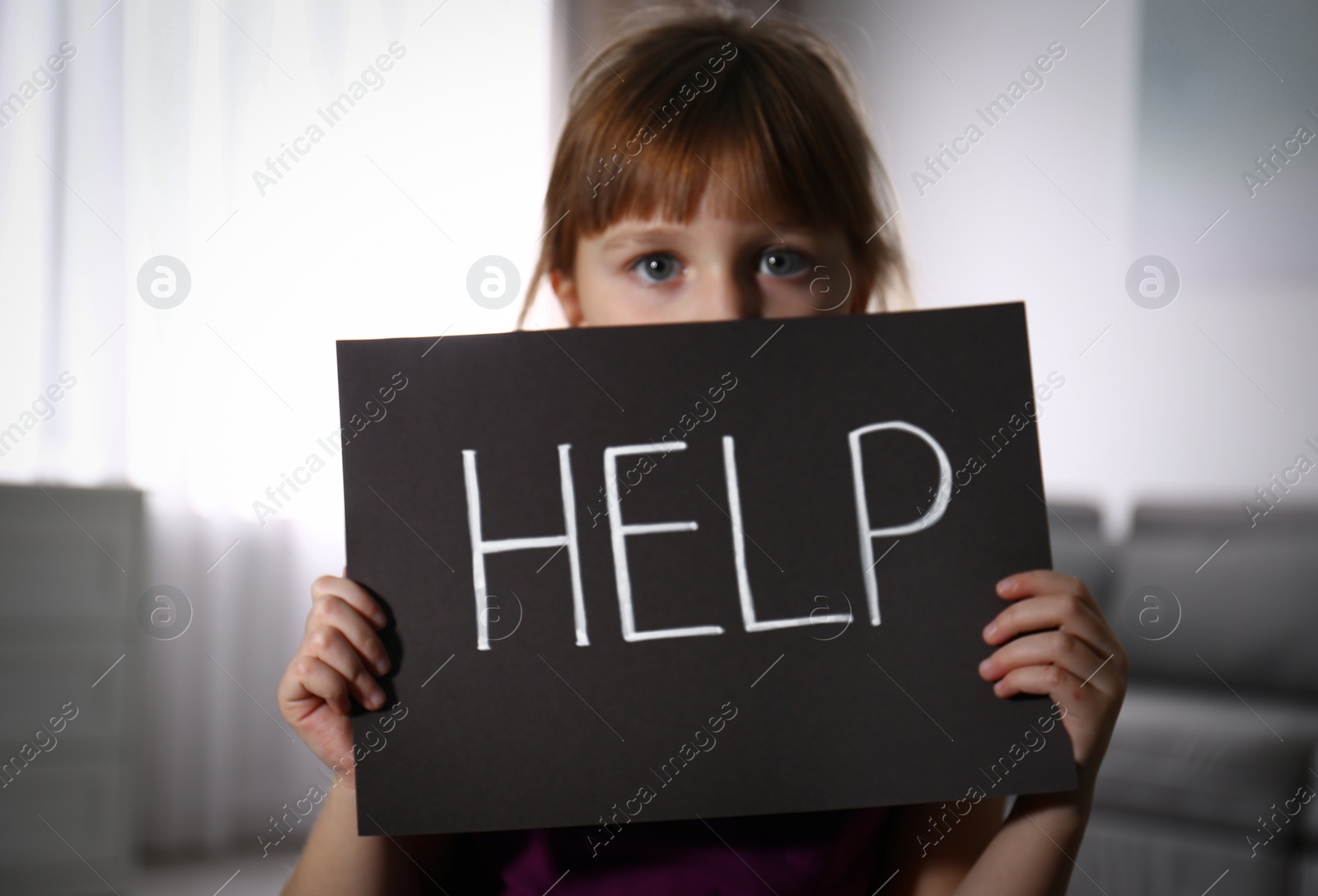 Photo of Abused little girl with sign HELP indoors. Domestic violence concept