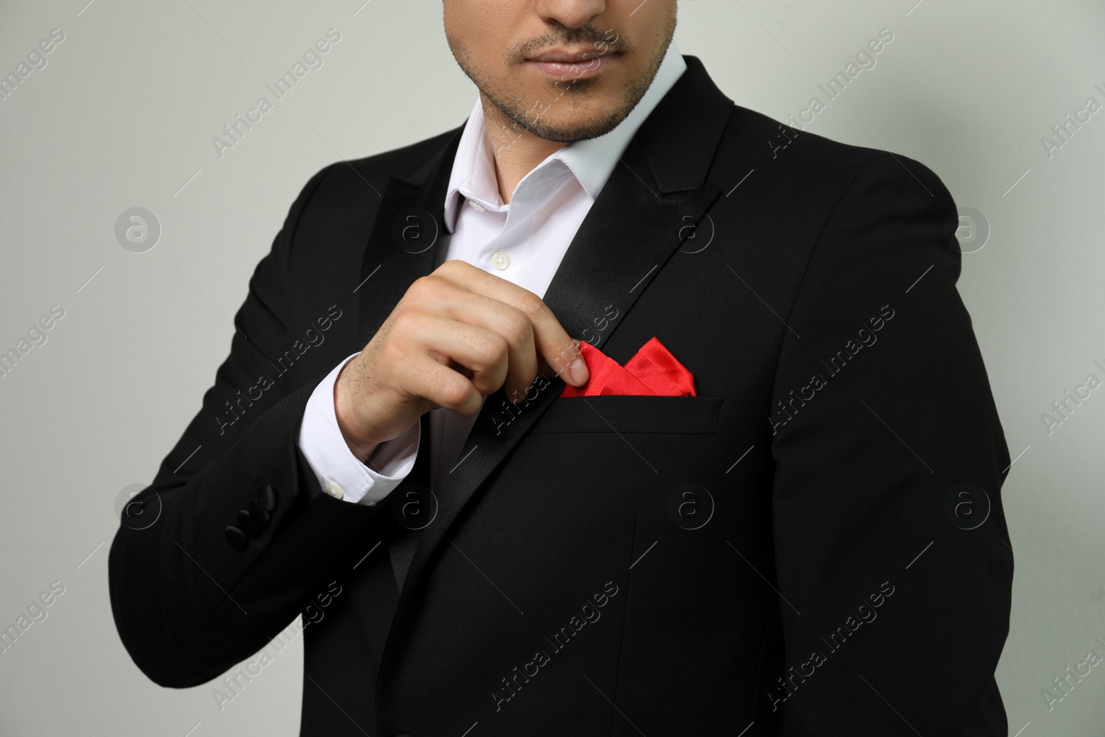 Photo of Man fixing handkerchief in breast pocket of his suit on light background, closeup