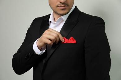 Man fixing handkerchief in breast pocket of his suit on light background, closeup