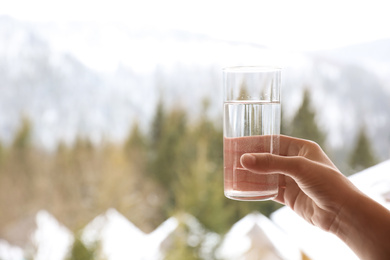 Woman holding glass of water outdoors on winter morning, closeup. Space for text