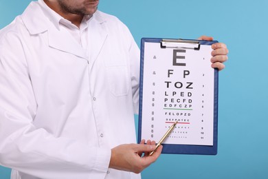 Photo of Ophthalmologist pointing at vision test chart on light blue background, closeup