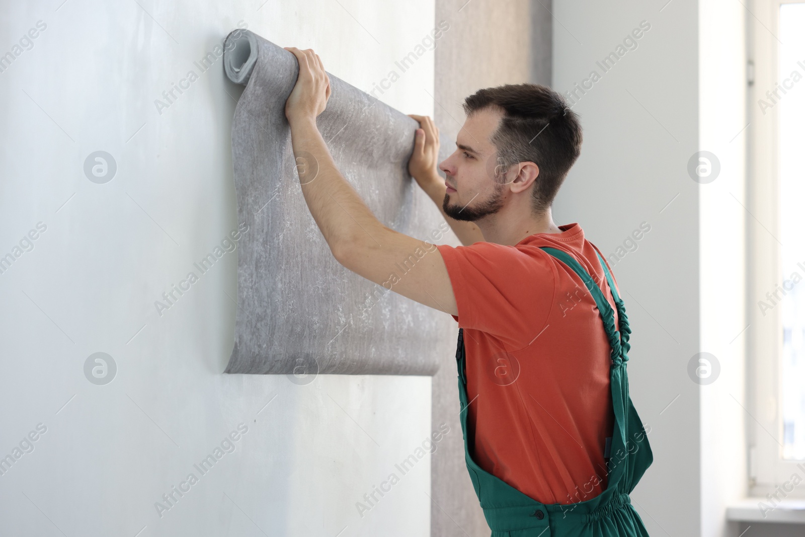 Photo of Man hanging stylish gray wallpaper in room