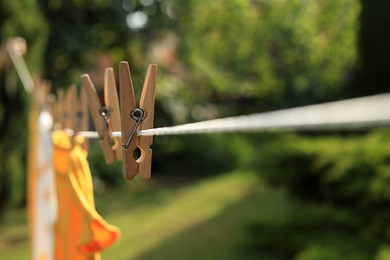 Photo of Clean clothes drying outdoors during sunny day, focus on laundry line with wooden clothespins