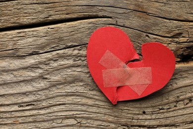 Broken heart. Torn red paper heart with medical adhesive bandages on wooden table, top view. Space for text