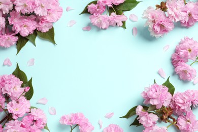 Photo of Beautiful frame of sakura tree blossoms on turquoise background, flat lay. Space for text