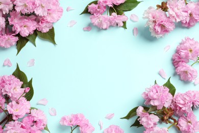 Beautiful frame of sakura tree blossoms on turquoise background, flat lay. Space for text