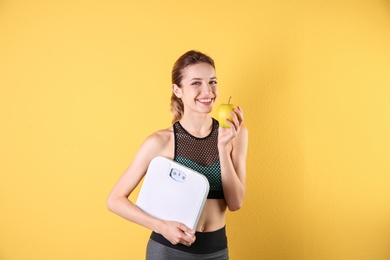 Photo of Young beautiful woman with scales and apple on color background. Weight loss motivation