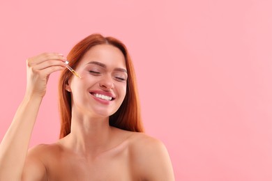 Photo of Beautiful young woman applying cosmetic serum onto her face on pink background, space for text