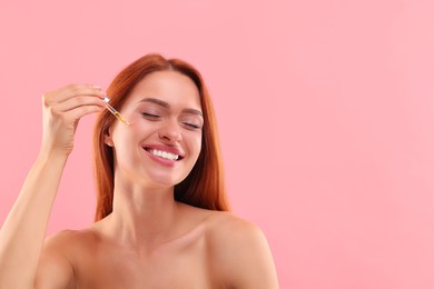 Beautiful young woman applying cosmetic serum onto her face on pink background, space for text