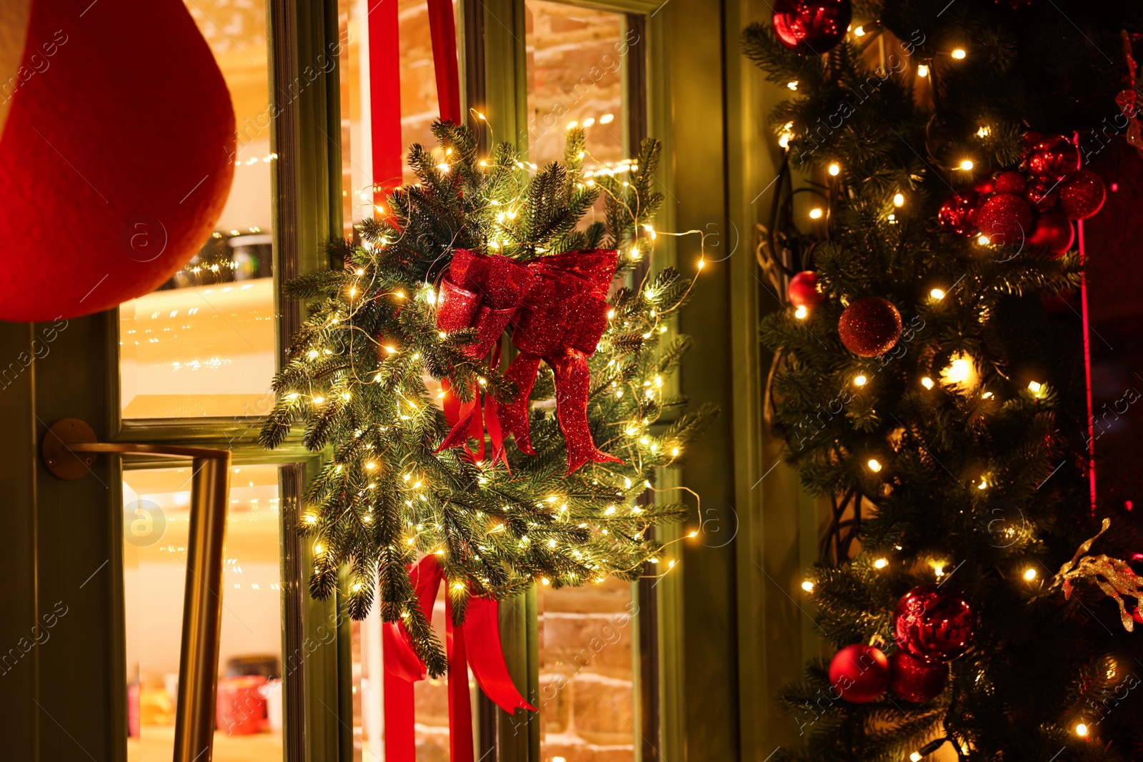 Photo of Beautiful Christmas wreath with ribbons and festive lights hanging on door