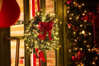 Beautiful Christmas wreath with ribbons and festive lights hanging on door