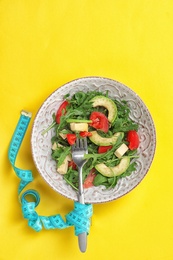 Photo of Bowl with fresh vegetable salad and measuring tape on color background, top view. Healthy diet