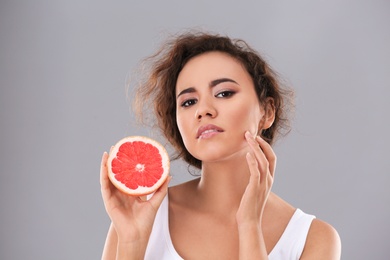 Photo of Beautiful young woman with acne problem holding grapefruit on grey background. Skin allergy