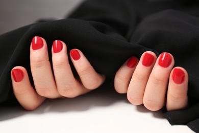 Photo of Woman with red manicure holding black fabric on white surface, closeup. Nail polish trends