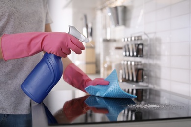 Young woman cleaning stove with rag in kitchen, closeup