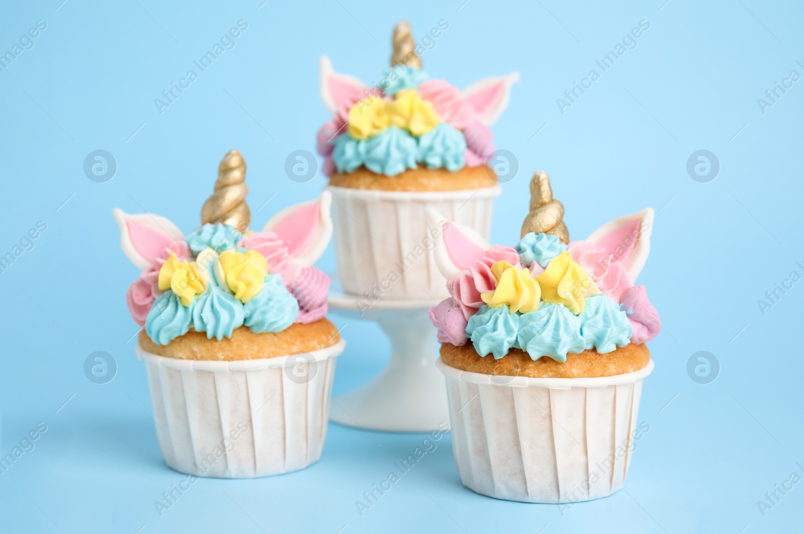 Photo of Cute sweet unicorn cupcakes on light blue background