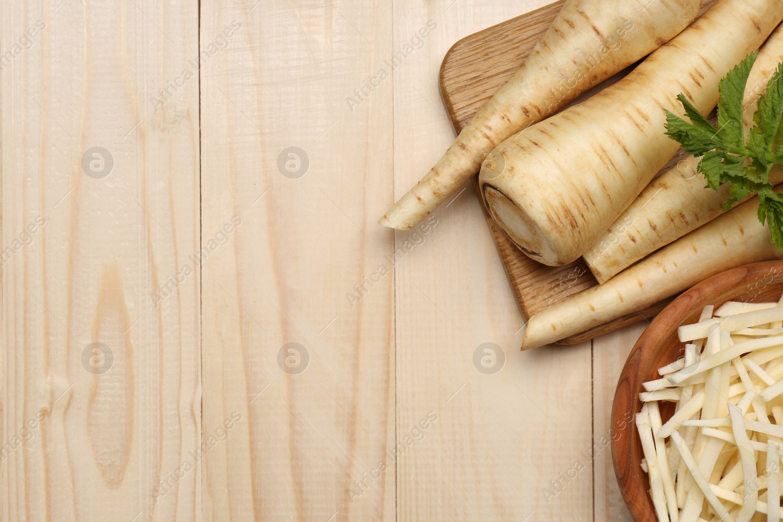 Photo of Whole and cut fresh ripe parsnips on wooden table, flat lay. Space for text