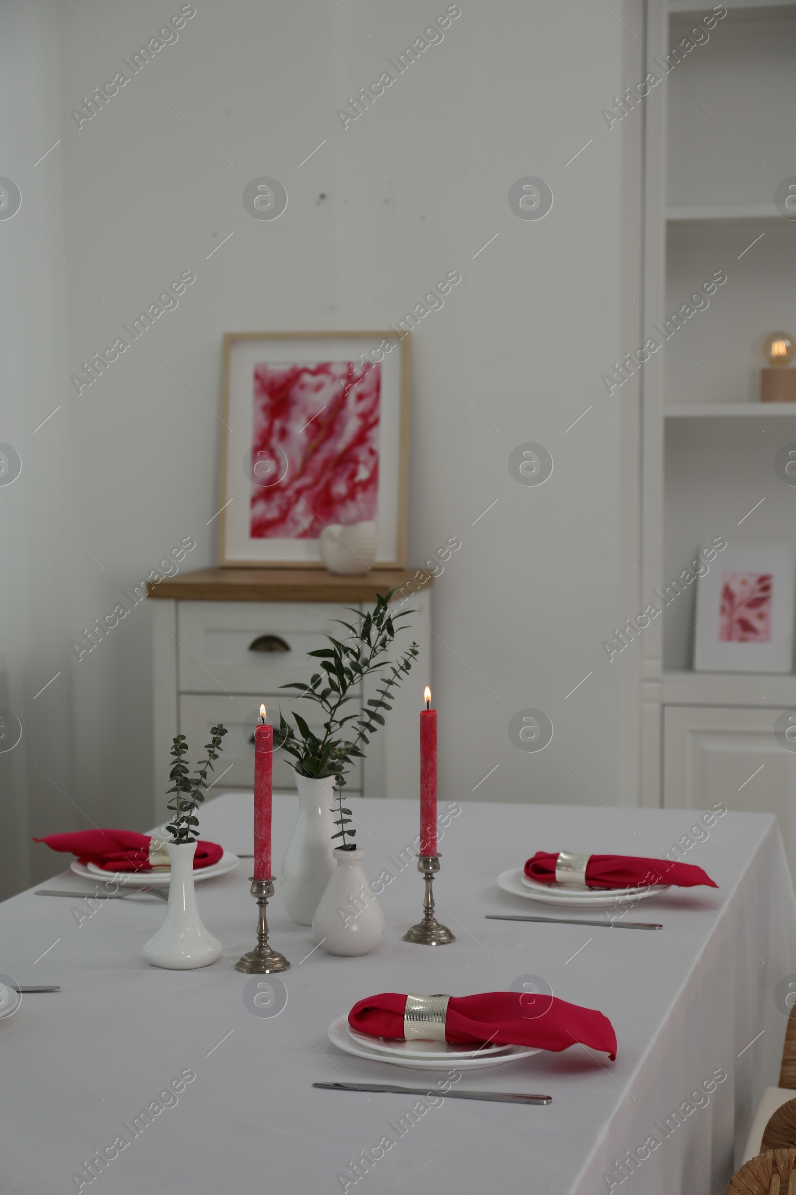 Photo of Beautiful table setting with green branches in vases and burning candles indoors. Stylish dining room