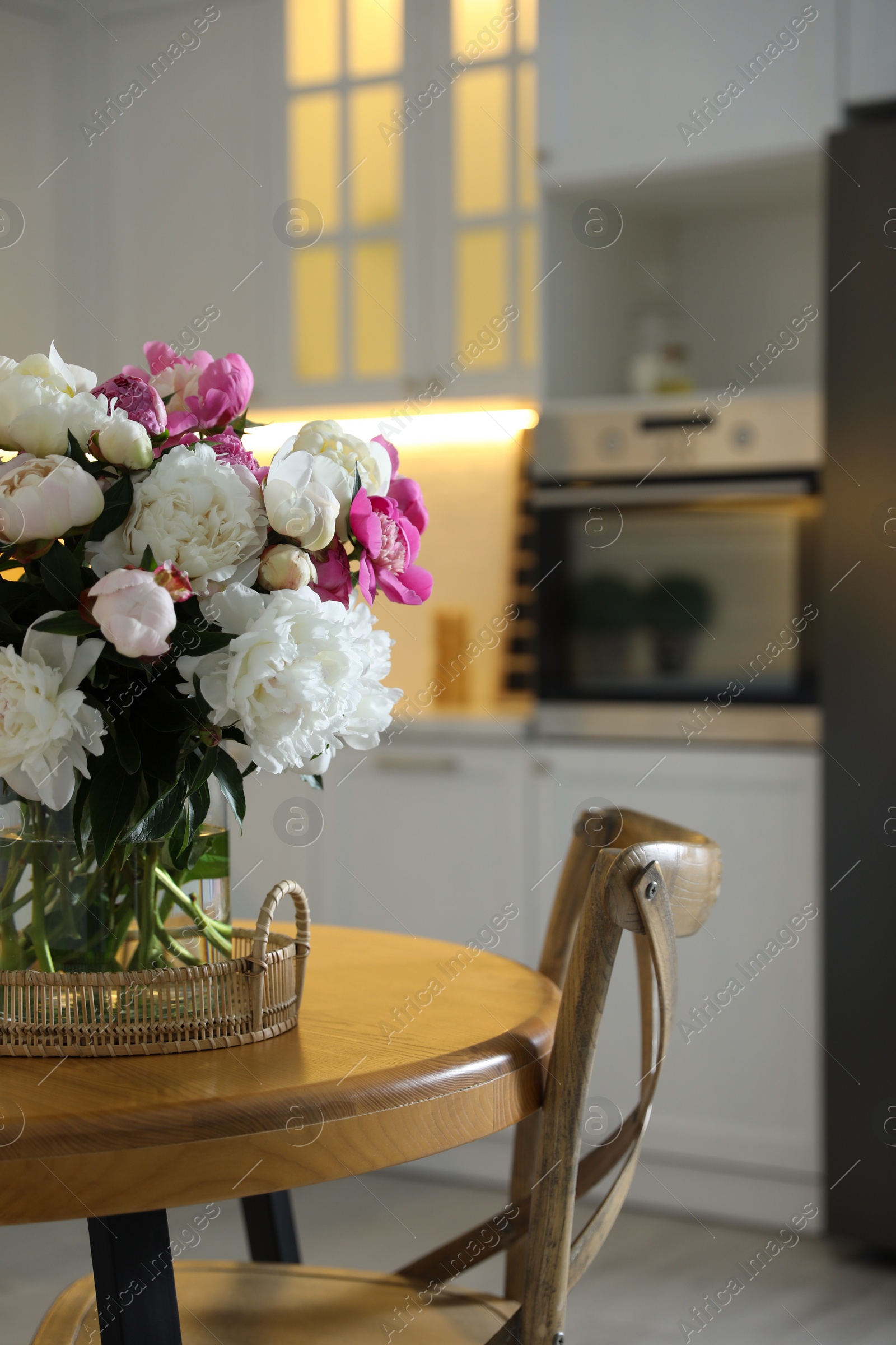 Photo of Beautiful peonies in vase on wooden table in kitchen
