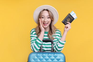 Happy young woman with passport, ticket and suitcase on yellow background