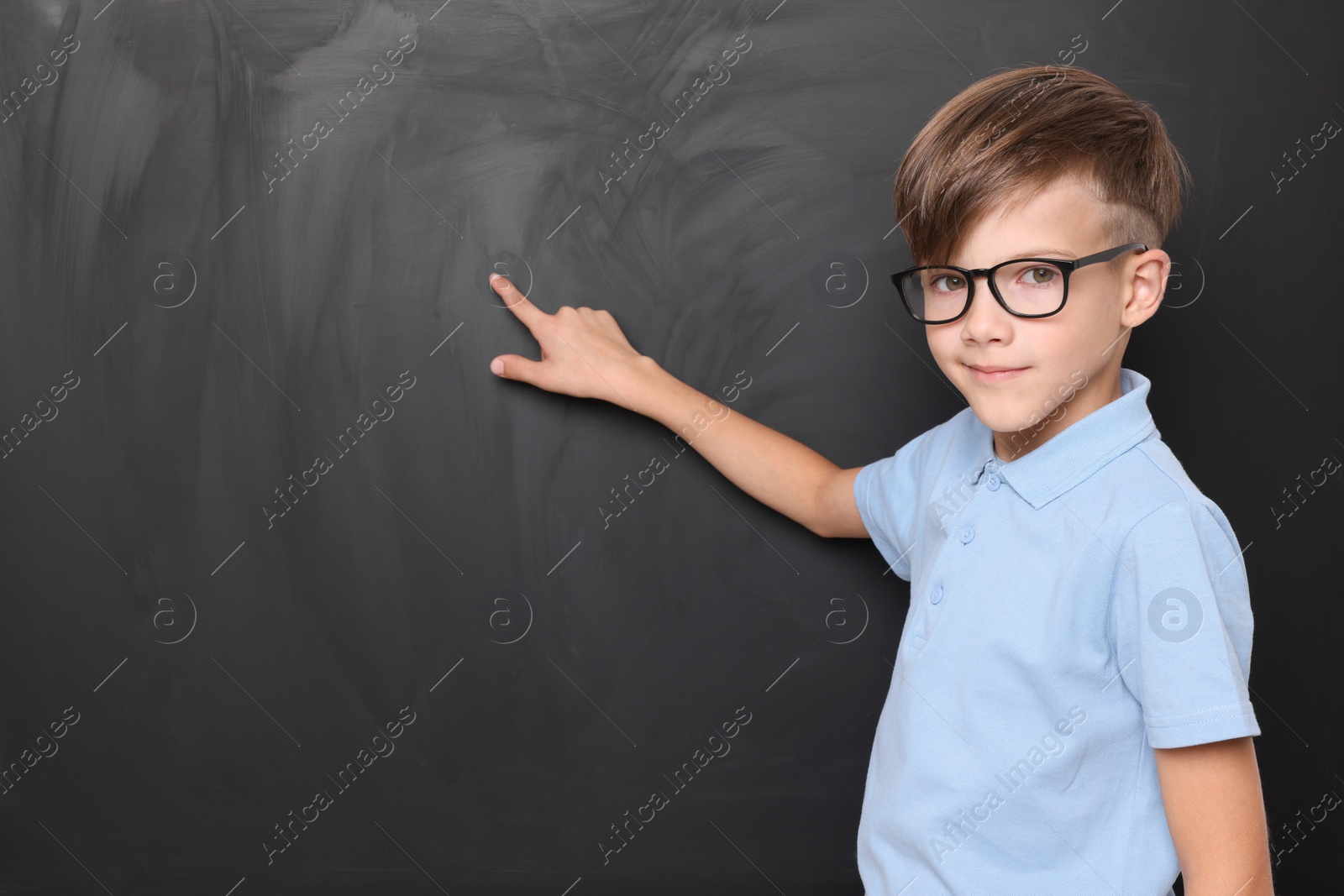 Photo of Cute schoolboy in glasses near chalkboard, space for text