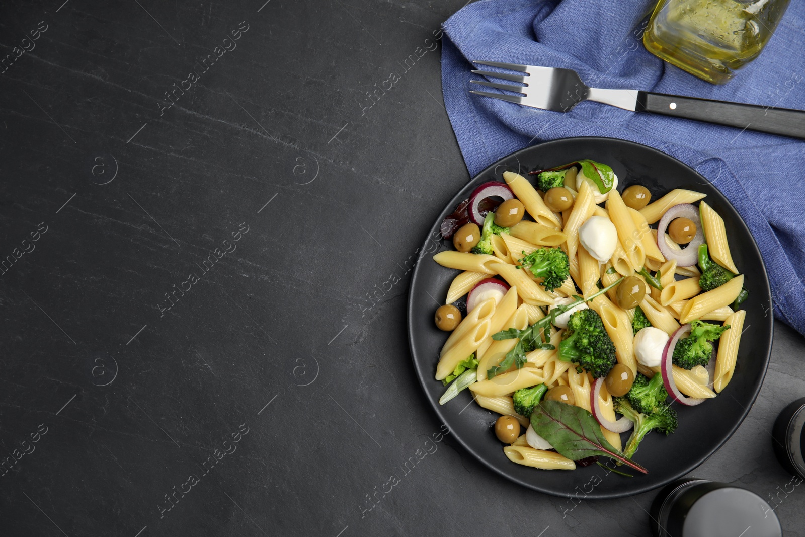 Photo of Plate of delicious pasta with broccoli, onion and olives on black table, flat lay. Space for text