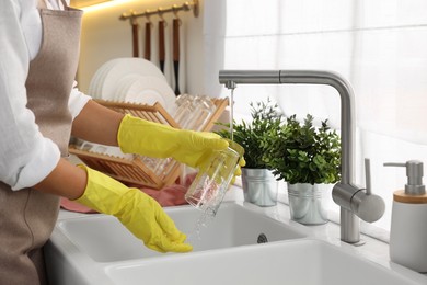 Photo of Woman washing glass at sink in kitchen, closeup