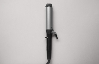 Hair curling iron on grey background, top view