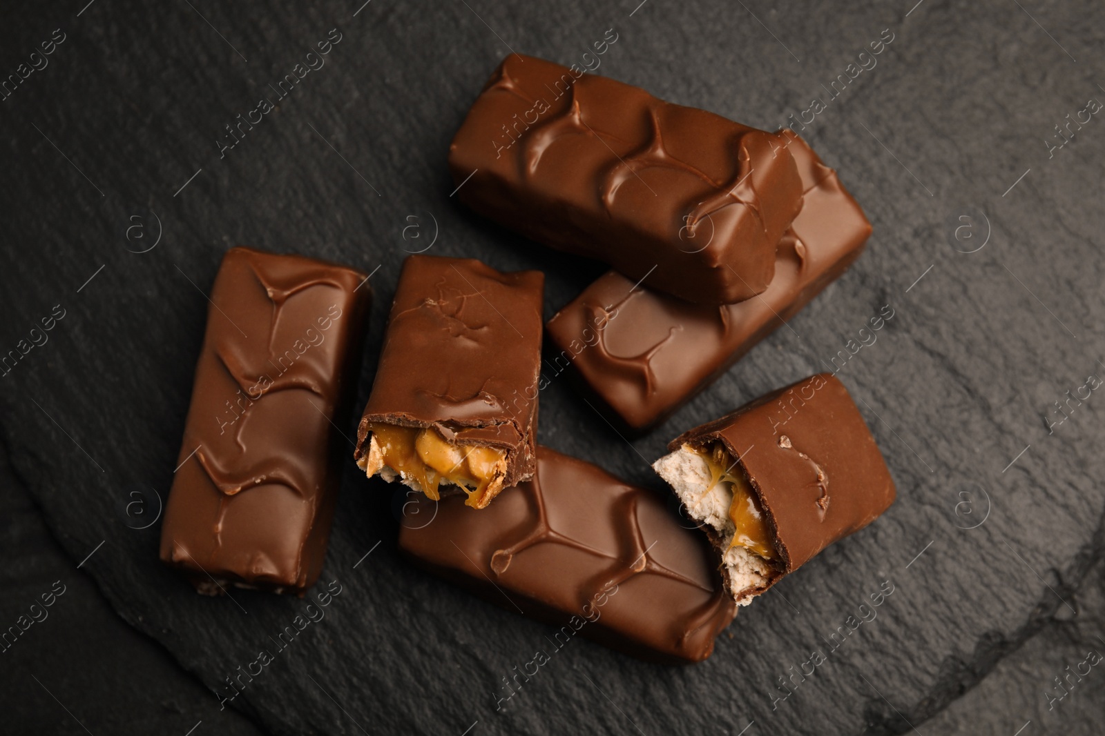 Photo of Chocolate bars with caramel, nuts and nougat on slate plate, top view