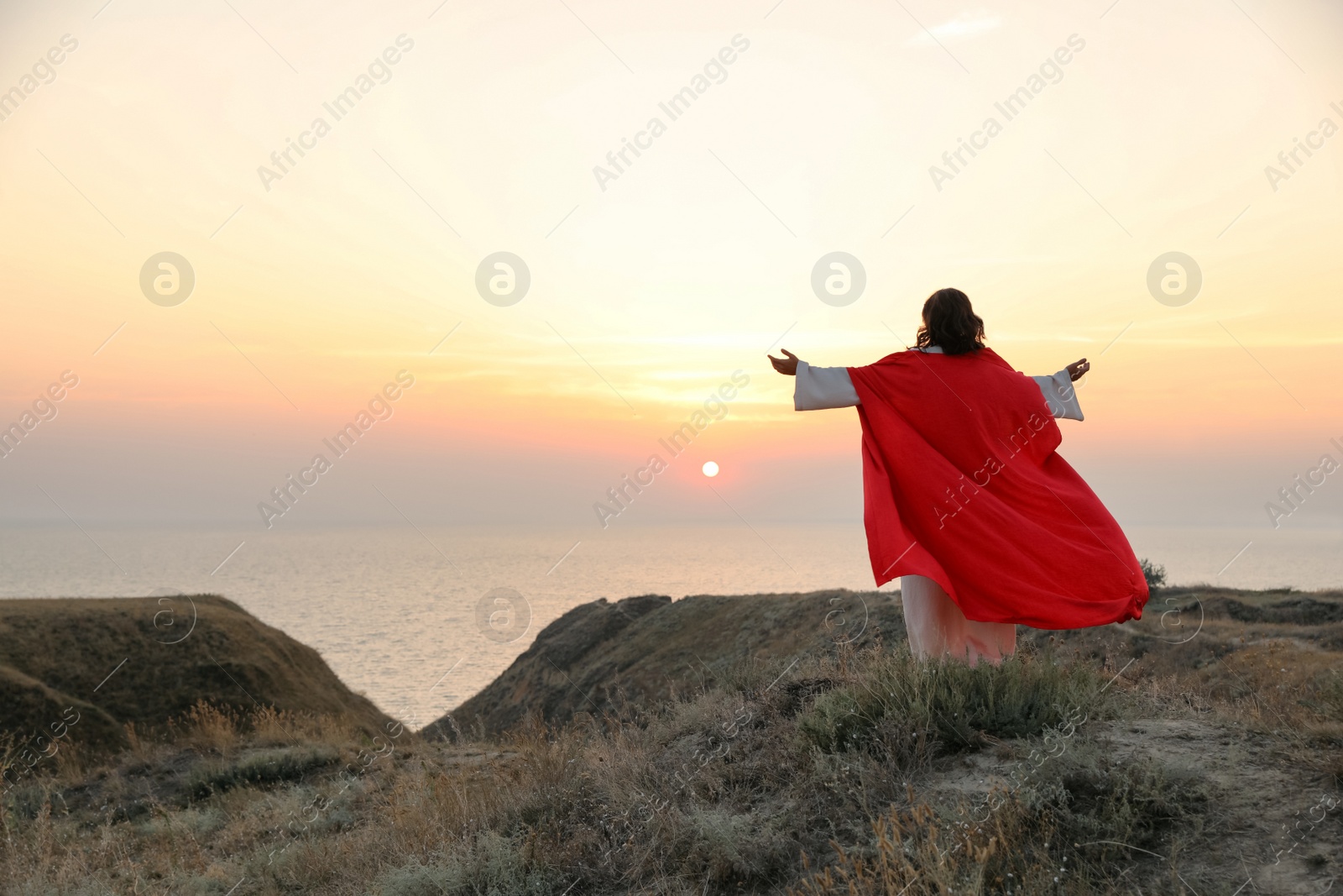 Photo of Jesus Christ raising hands on hills at sunset, back view. Space for text