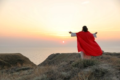 Photo of Jesus Christ raising hands on hills at sunset, back view. Space for text